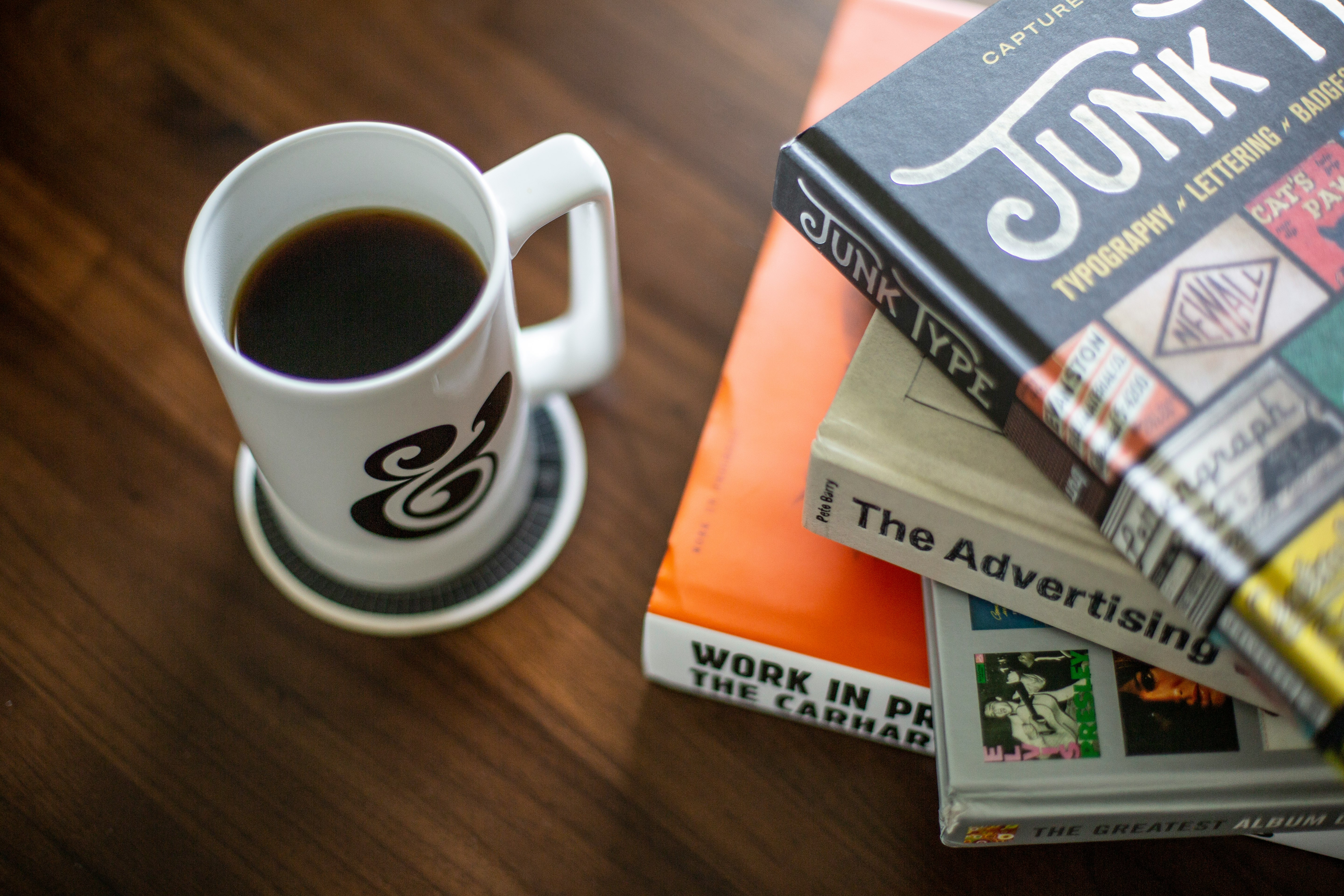 white and black coffee mug near pile of books on brown wooden surface
